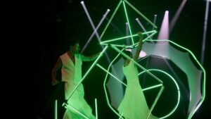 Geometric object manipulation with a glowing LED cube and LED tetrahedron in a circus setting.
